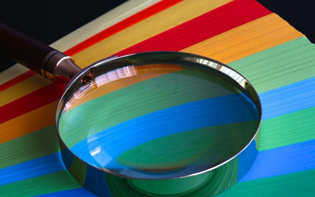 Magnifying glass resting on vibrant rainbow-colored paper close-up.