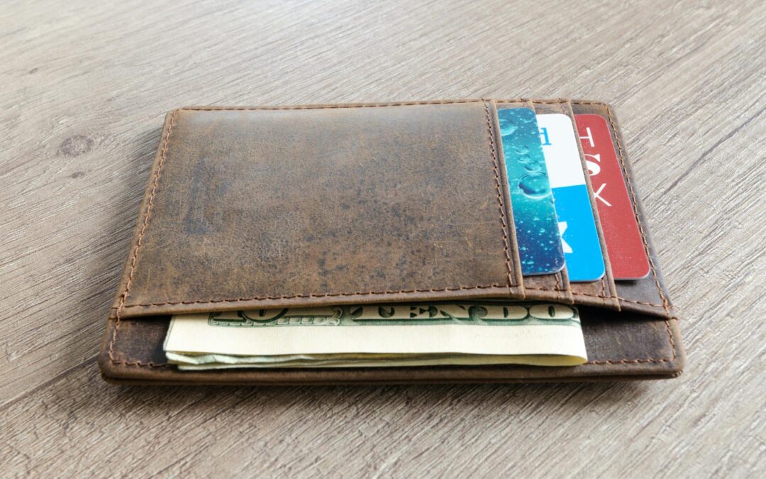 A brown leather wallet with cash and credit cards on a wooden surface.