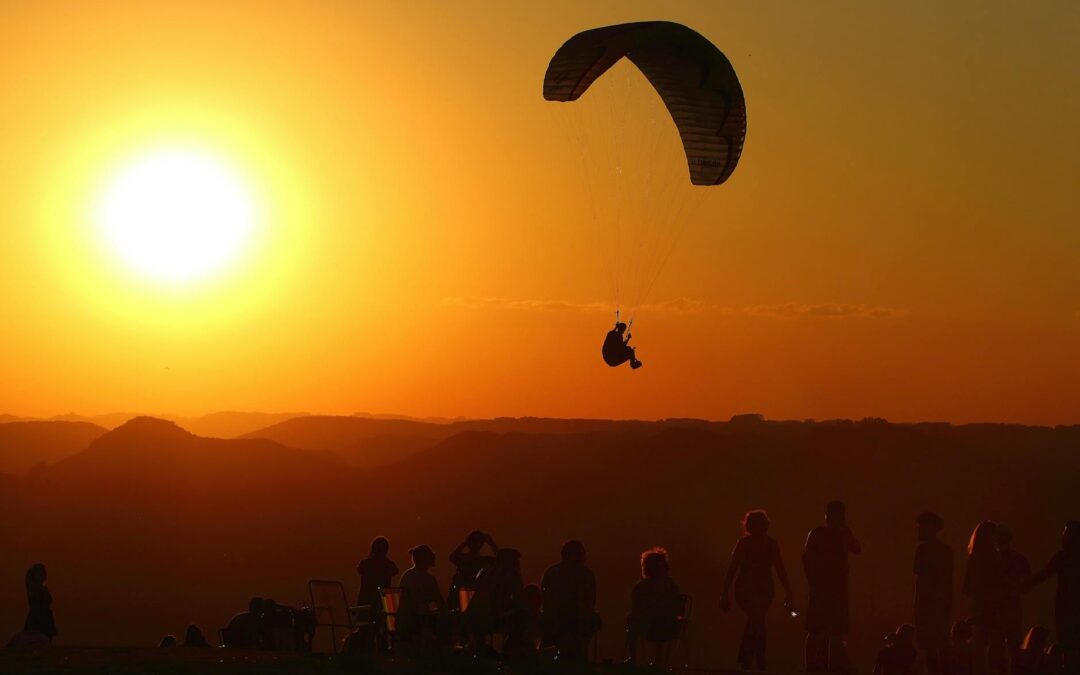 Silhouette of a paraglider and spectators enjoying a vibrant sunset in Brazil.