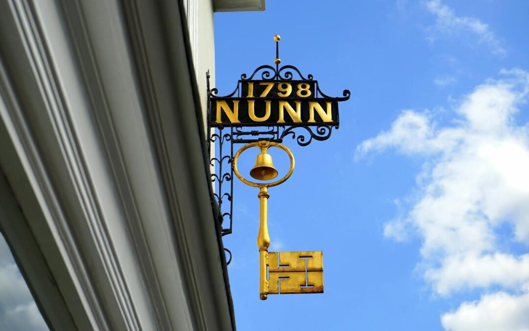 Ornate metal sign with key and bell at vintage building facade under clear skies.