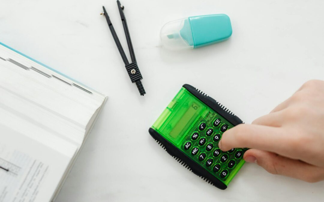 Close-up of a hand using a green calculator with stationery for studies or business calculations.